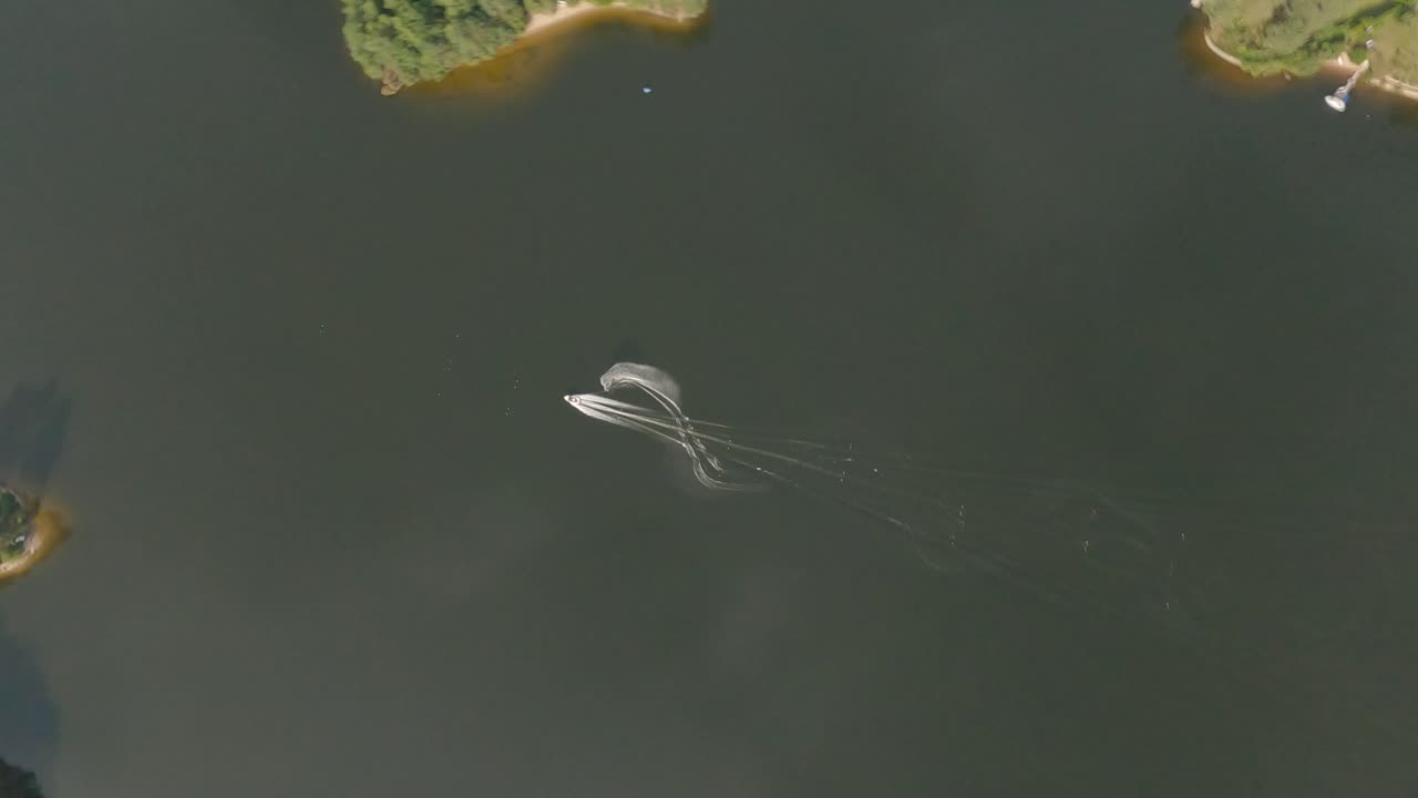 Aerial view top-down FPV of speedboat making figure eight turns on lake, Marcillac La Croisille, France