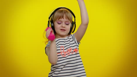 child girl listening music via headphones, working out pumping up arm muscles lifting pink dumbbells