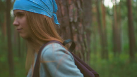 young hikers pause in serene forest, hanging their bags over their shoulders while surrounded by tall trees and lush greenery, one hiker with long hair and a blue bandana holds her bag gracefully