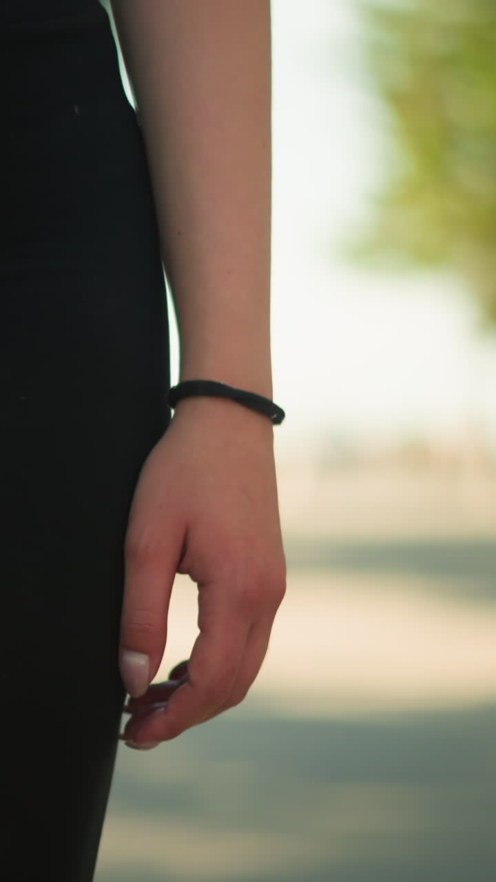 vista inferior del cuerpo de una mujer con ropa deportiva negra caminando al aire libre con un brazalete de mano negro, con un primer plano del brazo y un fondo borroso de vegetación exuberante, bajo la cálida luz del sol