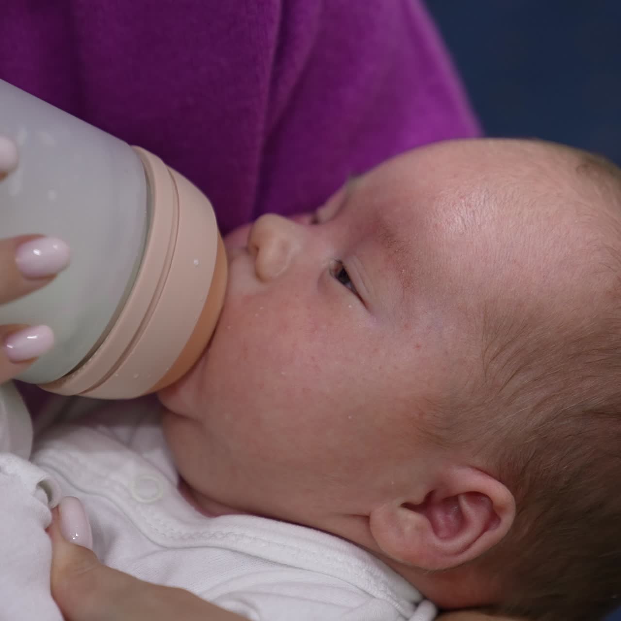 Baby lying in mommy's hands ready to be fed. Baby grasping the pacifier of the bottle and suckling hungrily. Close up