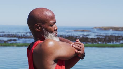 hombre afroamericano de alto nivel haciendo ejercicios de estiramiento en rocas junto al mar