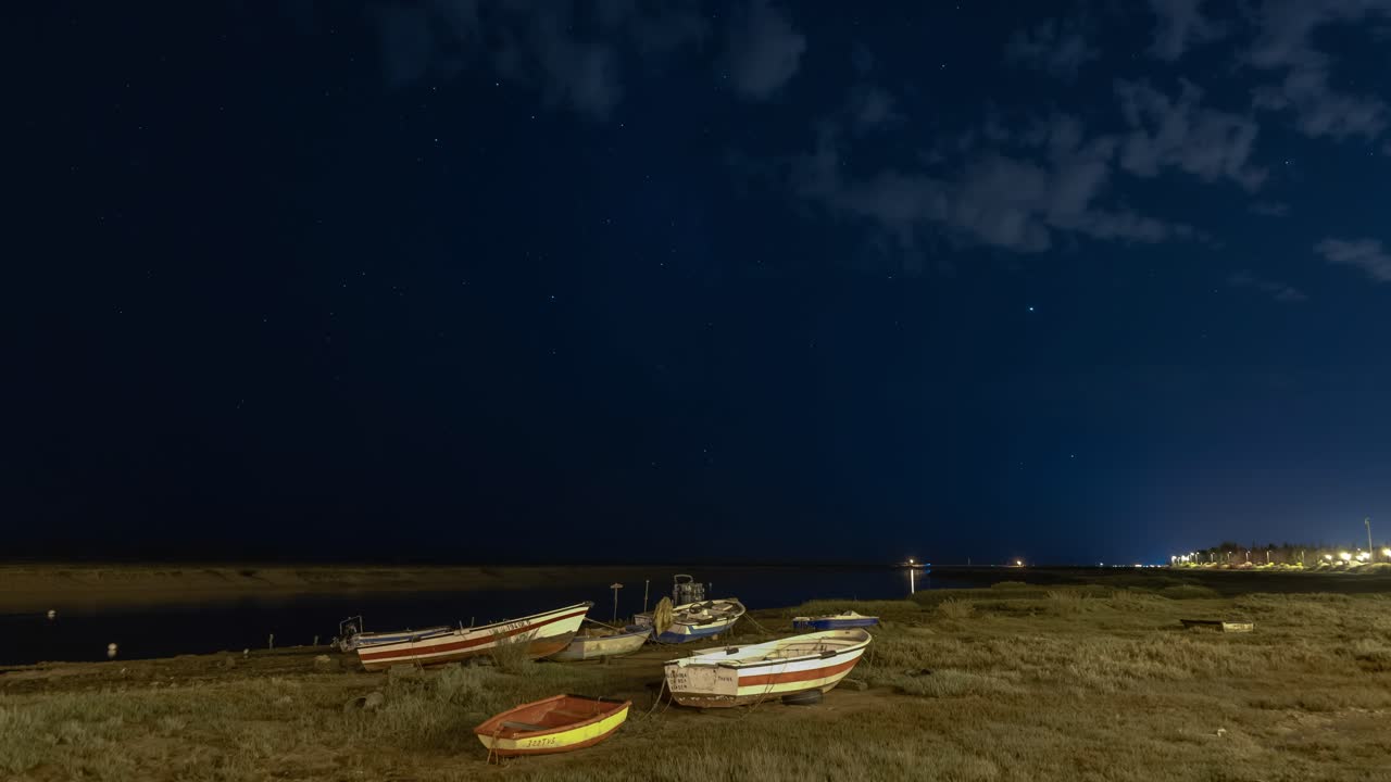 Timelapse de estrelas noturnas com barcos em terra