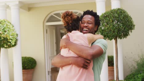feliz pareja biracial abrazándose con alegría frente a la nueva casa