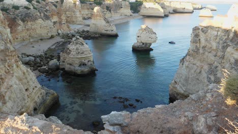 tiro inclinado lentamente, vista panorámica de la playa de túneles de roca en algarve, portugal, gente caminando en la playa y barco flotando cerca de la formación rocosa en el mar