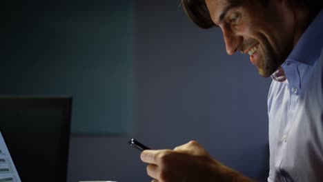 Side-view-of-young-Caucasian-male-executive-using-mobile-phone-while-working-on-laptop-in-office-4k