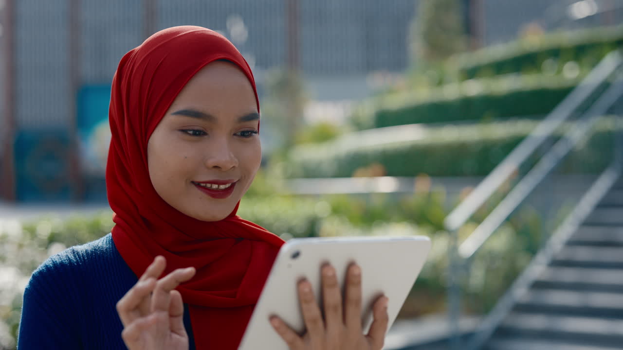 A young Muslim woman in a red hijab uses a tablet outdoors