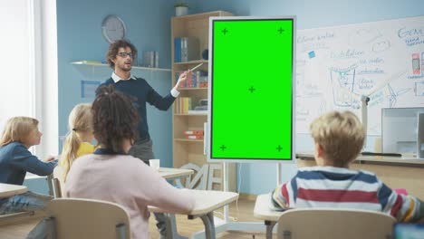 in the elementary school classroom: teacher uses vertical green mock-up screen interactive digital whiteboard to explain lesson to diverse group of schoolchildren. multi ethnic kids learning science