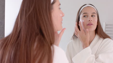 applying face cream, woman looking in mirror during home spa routine