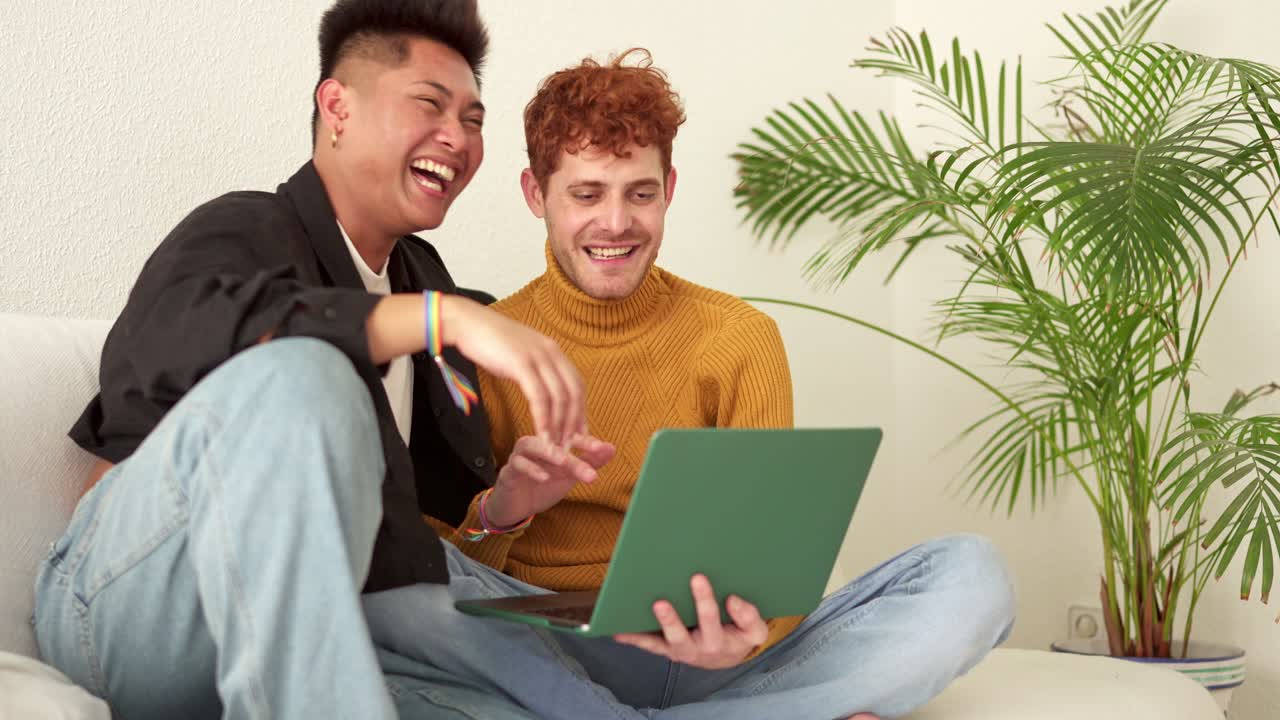 Happy gay couple laughing while using a laptop at home