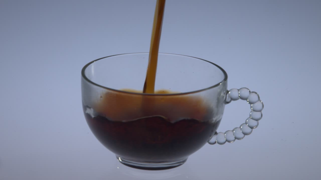 Pouring coffee into a clear white coffee cup in slow motion