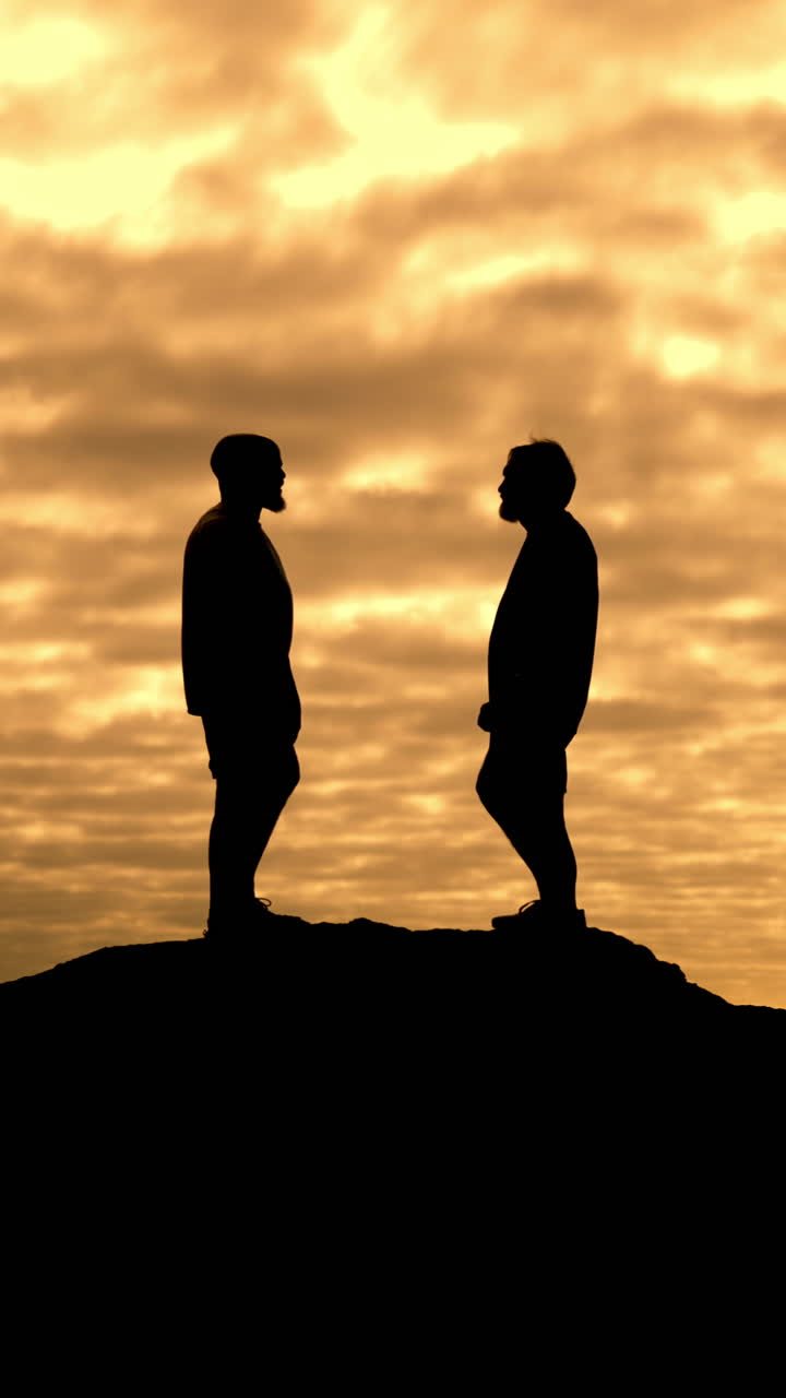 Due uomini in silhouette che parlano in cima a una collina al tramonto