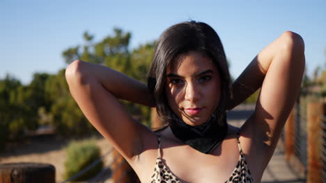 a beautiful young hispanic woman fashion model tying a bandana and staring in an outdoor desert landscape slow motion