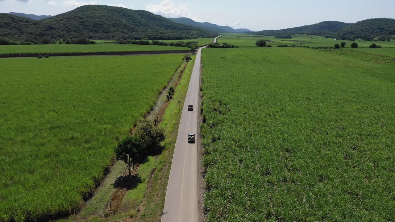 aerial of two cars driving on long road, tilt view reveals mountains in horizon