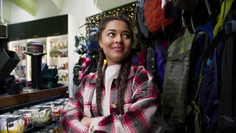 portrait of young attractive girl standing in sport goods store with backpacks on background