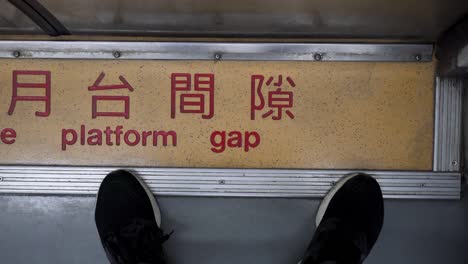 one person stands in front of the door in the train carriage. close-up feet. the chinese word means mind the platform gap. the train is moving and the camera shakes. the subject is on the right.