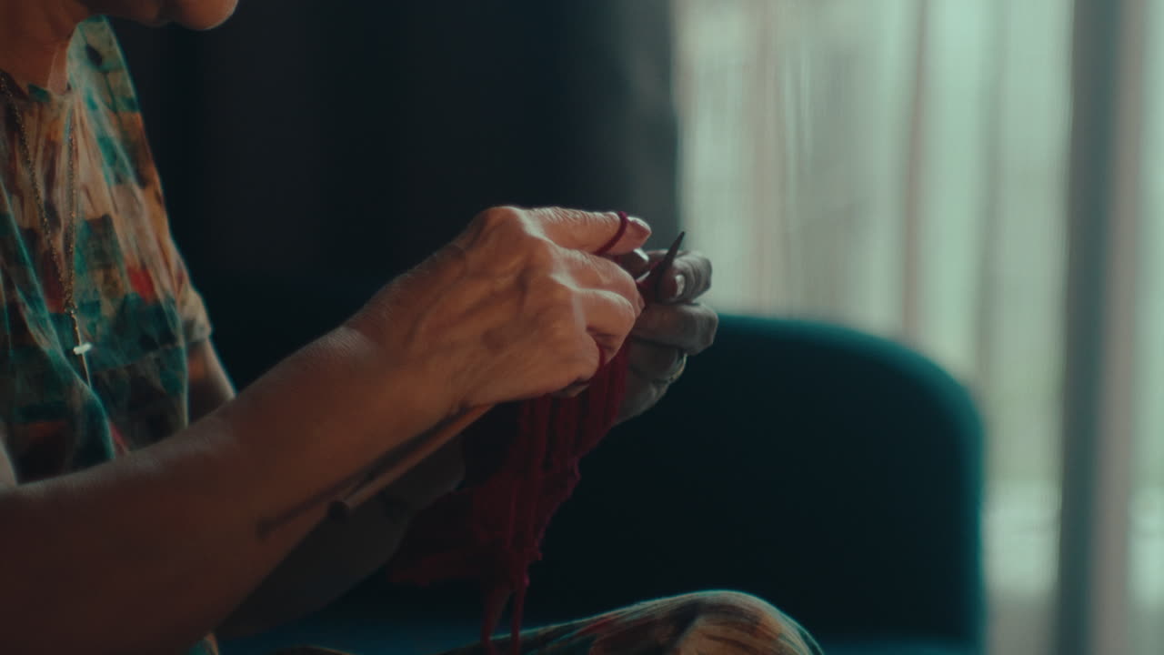 mujeres mayores creativas y hábiles manos cercanas mientras hacen ganchillo con una rápida combinación de movimientos sentadas solas en casa