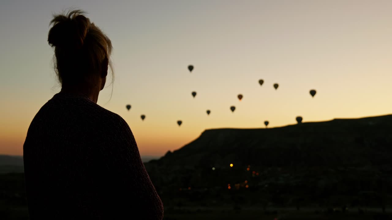 mujer con silueta mira hacia el cielo al amanecer globos de aire caliente