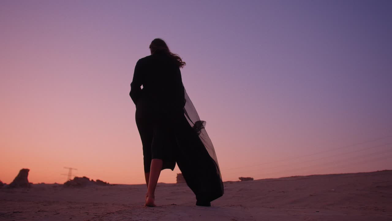 Carrellata di una ragazza araba che vaga nel deserto con dune fossili sullo sfondo durante un bellissimo tramonto.