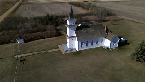 drone orbiting around old country church in alberta's prairies while slowly ascending and revealing young person walking along a path towards the building