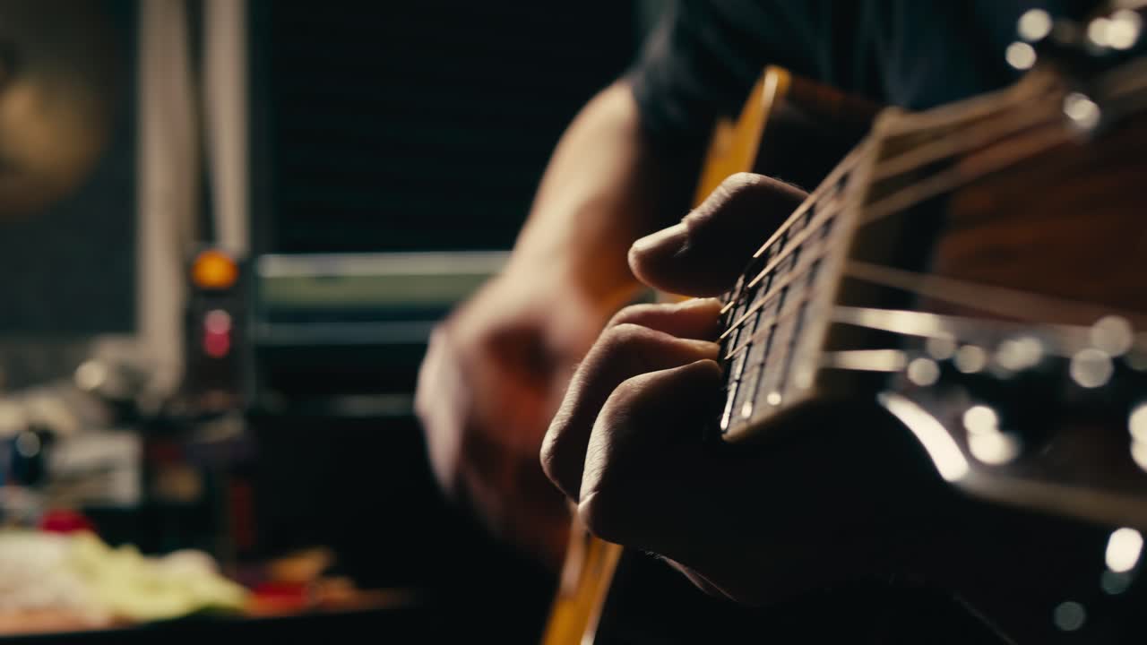 Young musican man checking strings of acoustic guitar close-up. Male guitarist tuning sound of musical instrument.
