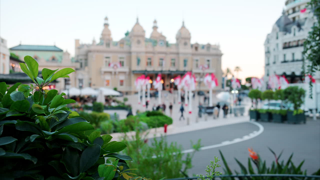 Distant, blurry street view of multiple Monegasque flags waving in front of the Monte Carlo Casino