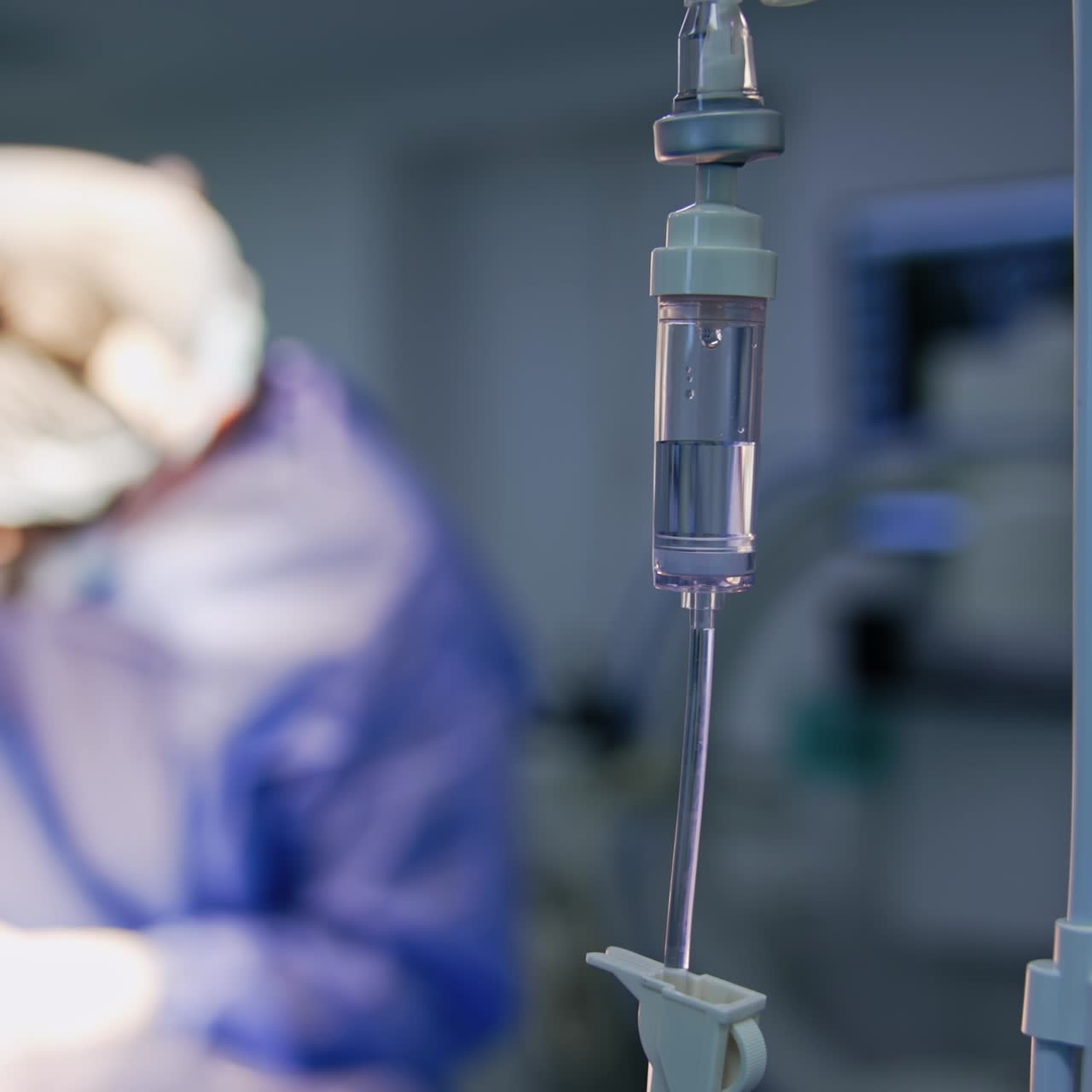 Soluzione salina all'interno del serbatoio della flebo. Medici che operano il paziente sullo sfondo in modalità sfocata