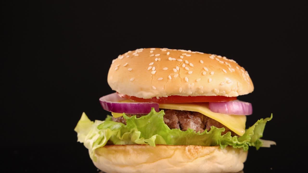 A classic beef burger with lettuce, tomato, onion, and sesame seed bun rotates smoothly against a black backdrop under bright, even studio lighting