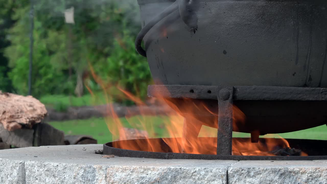 야외 벽난로에서 불이 타오르고 오래된 쇠주전자를 데우고 있다