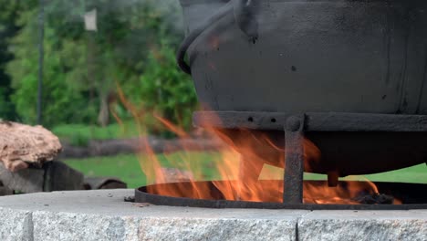 un fuego ardiendo en una chimenea al aire libre y calentando una vieja tetera de hierro