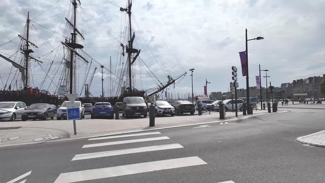 Walking on the street of Saint Malo with fortified city in view and towards mastes of a pirate ship, Brittany, France.