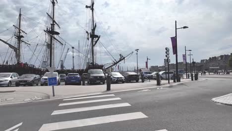 walking on the street of saint malo with fortified city in view and towards mastes of a pirate ship, brittany, france.