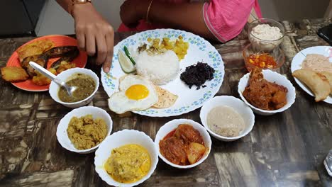 an indian meal with rice egg vegetable and different type of  dessert in a large plate and small dishes being eaten at the occasion of baby shower