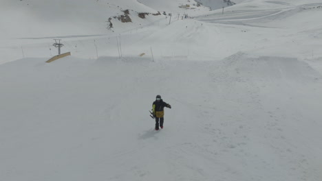snowboarder holding snowboard and walking uphill the pistes on the snowy slopes of mount hermon, golan heights, israel