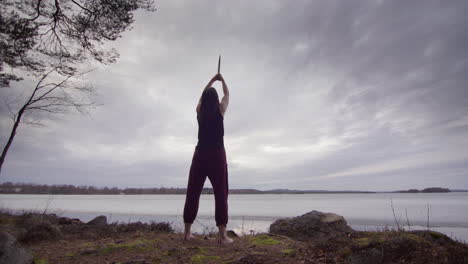 Arcing-hero-shot-of-powerful-woman-holding-sword-up-high-overlooking-frozen-lake