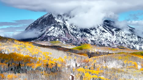 kebler pass aerial cinematic drone crested butte gunnison colorado seasons collide early fall aspen tree red yellow orange forest winter first snow powder rocky mountain peak dirt road forward motion