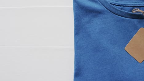 Video-of-flat-lay-of-blue-t-shirt-with-tag-and-copy-space-on-white-background