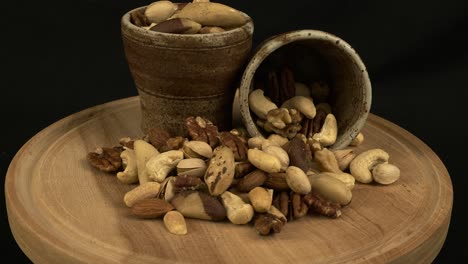 Rich brown nuts in cups on wooden board revolve on isolated black