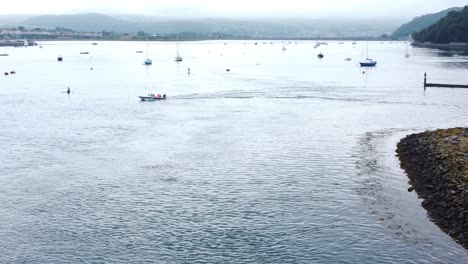 Vista-Aérea-De-Lancha-Dejando-El-Puerto-De-La-Ciudad-Costera-Galesa-Navegando-A-Lo-Largo-Del-Río-Conwy