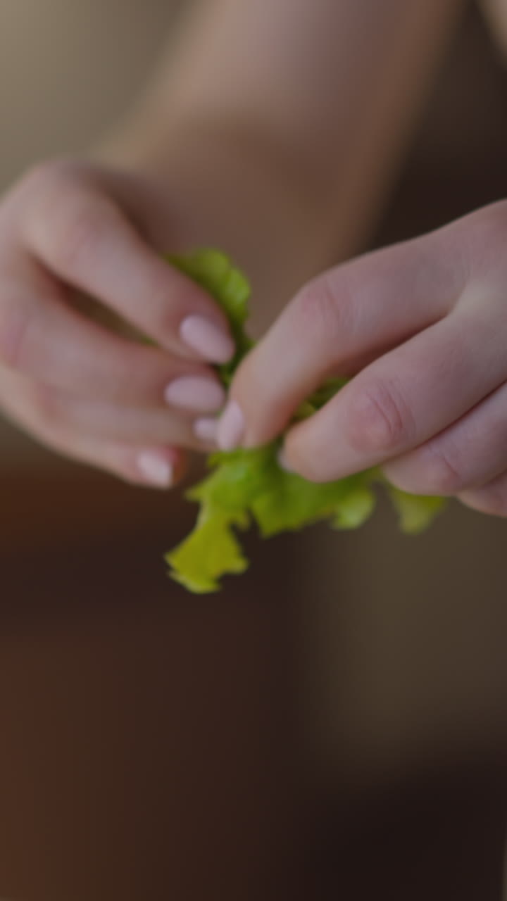 las manos de la mujer desgarran hojas de lechuga fresca preparando ensalada saludable para seguir la dieta en la mesa en la cocina ligera vista extrema de cerca cámara lenta