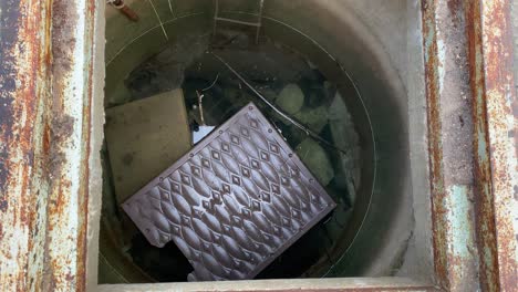 looking down into an open manhole showing sewer with waste water.