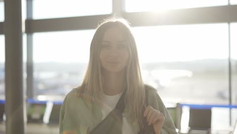 portrait of a stylish young blonde girl traveller stands in airport terminal in sunlight