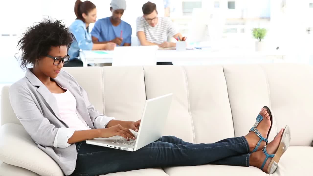 Pretty designer lying on couch working on laptop