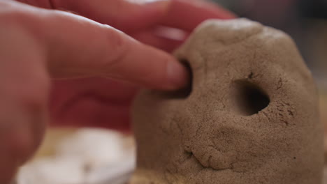 healing companion gently presses soft mold surface to shape eye of octopus figure during therapy activity, with blurred presence of seated figure in blue gown suggesting supportive session setting