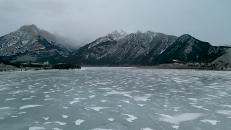 Kalter-Gefrorener-See-Mit-Nebligen-Schneebedeckten-Bergen-In-Der-Ferne