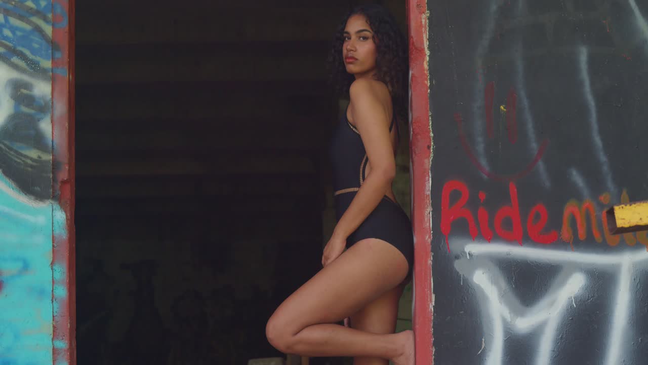 Woman in Black Swimsuit Posing in Abandoned Building with Graffiti