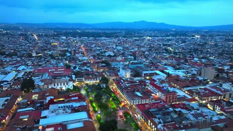 drone: dolly in tilt up shot of downtown uruapan after sunset on a cloudy day