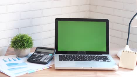 modern workspace with laptop, calculator, and green screen