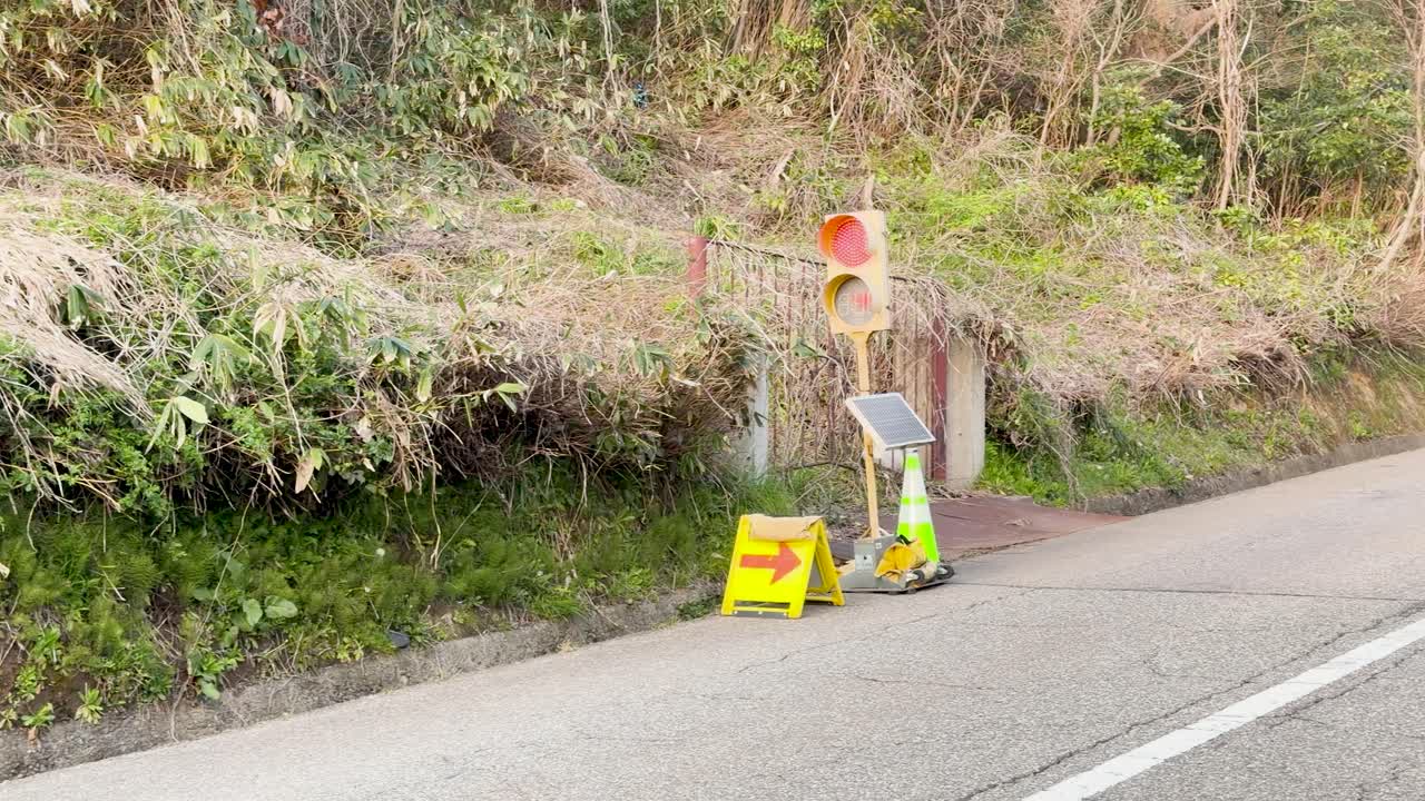 En sakte panorering avslører gule anleggsskilt og midlertidige trafikklys langs en åsside.