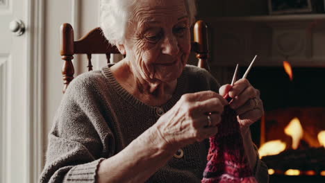 mujer anciana tejiendo junto a la chimenea